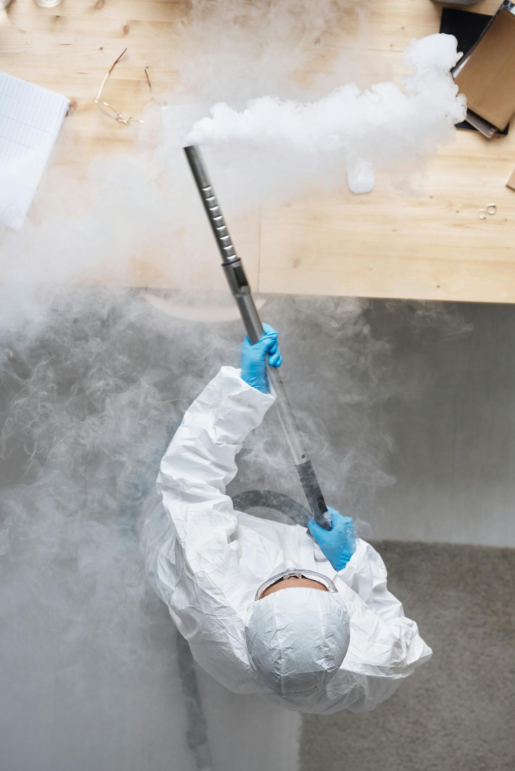 Person in Personal Protective Equipment Fumigating a Wooden Table